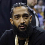FILE - Rapper Nipsey Hussle attends an NBA basketball game between the Golden State Warriors and the Milwaukee Bucks in Oakland, Calif., March 29, 2018. Three years after rapper Hussle was gunned down outside a Los Angeles clothing store that he founded to help revitalize the neighborhood where he grew up, a trial will finally begin Wednesday, June 15, 2022, for the man charged with killing him. (AP Photo/Marcio Jose Sanchez, File)